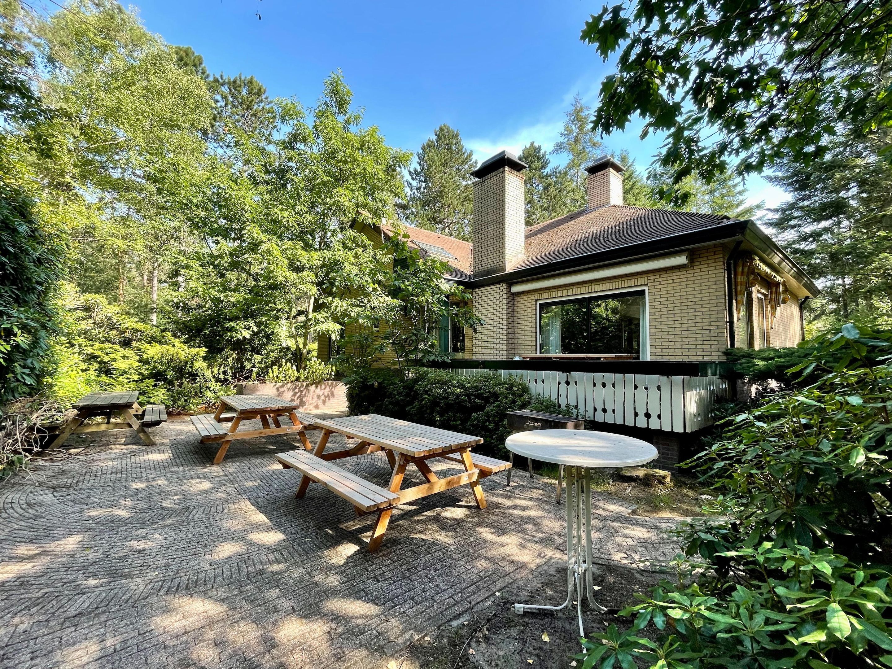 A rustic cabin with a brick exterior, surrounded by dense greenery and a wooden deck.
