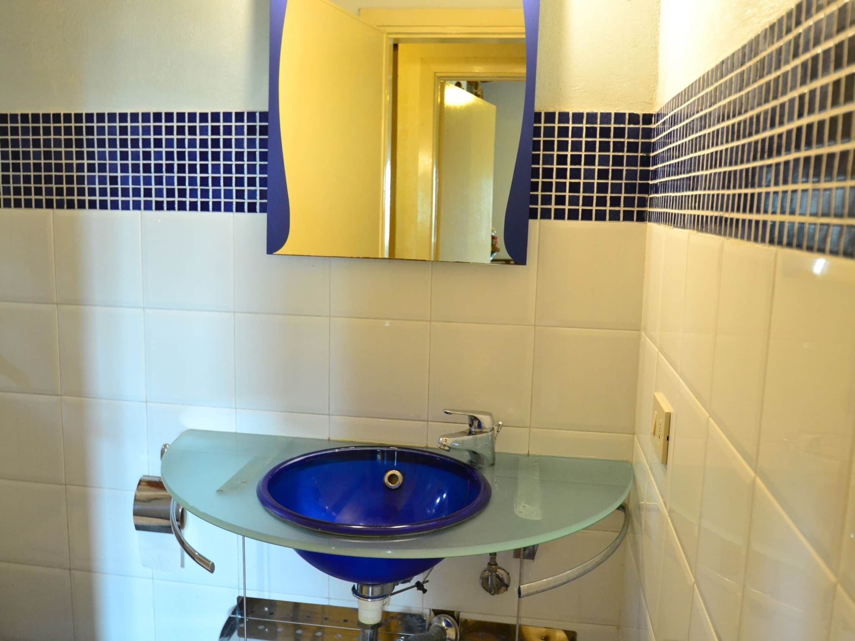 A bathroom with a glass sink, a mirror, and blue and white tiled walls.