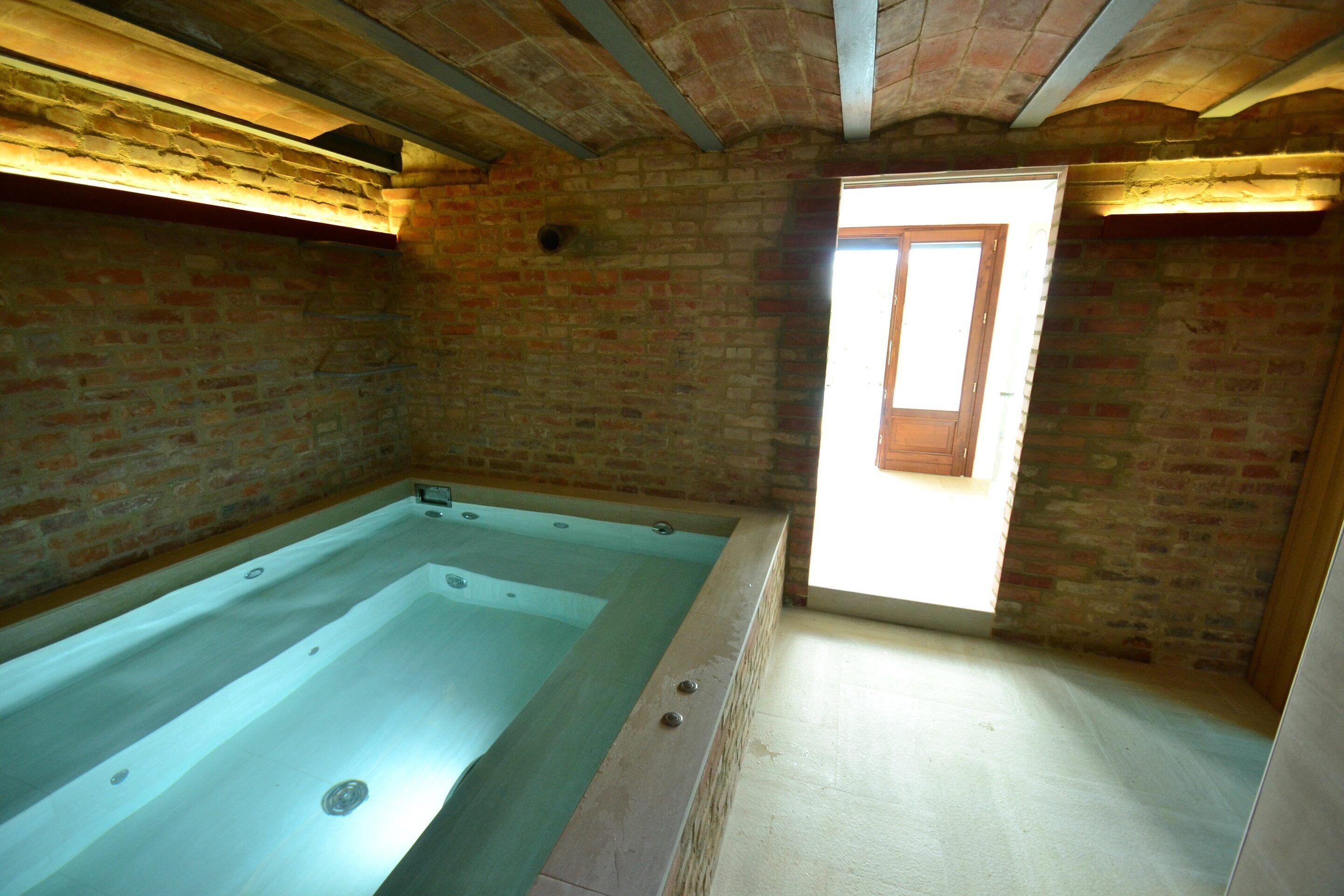 A spa room with a large bathtub, brick walls, and a wooden door.