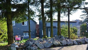 Ett bostadsområde med en asfalterad gångväg, en stenmur och ett hus med grå fasad och vita fönster.