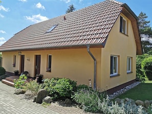 A two-story house with a tiled roof, a front porch, and a small garden with rocks and plants. - Spacious Appartment in Wilhelmshof Near Lake (Usedom)
