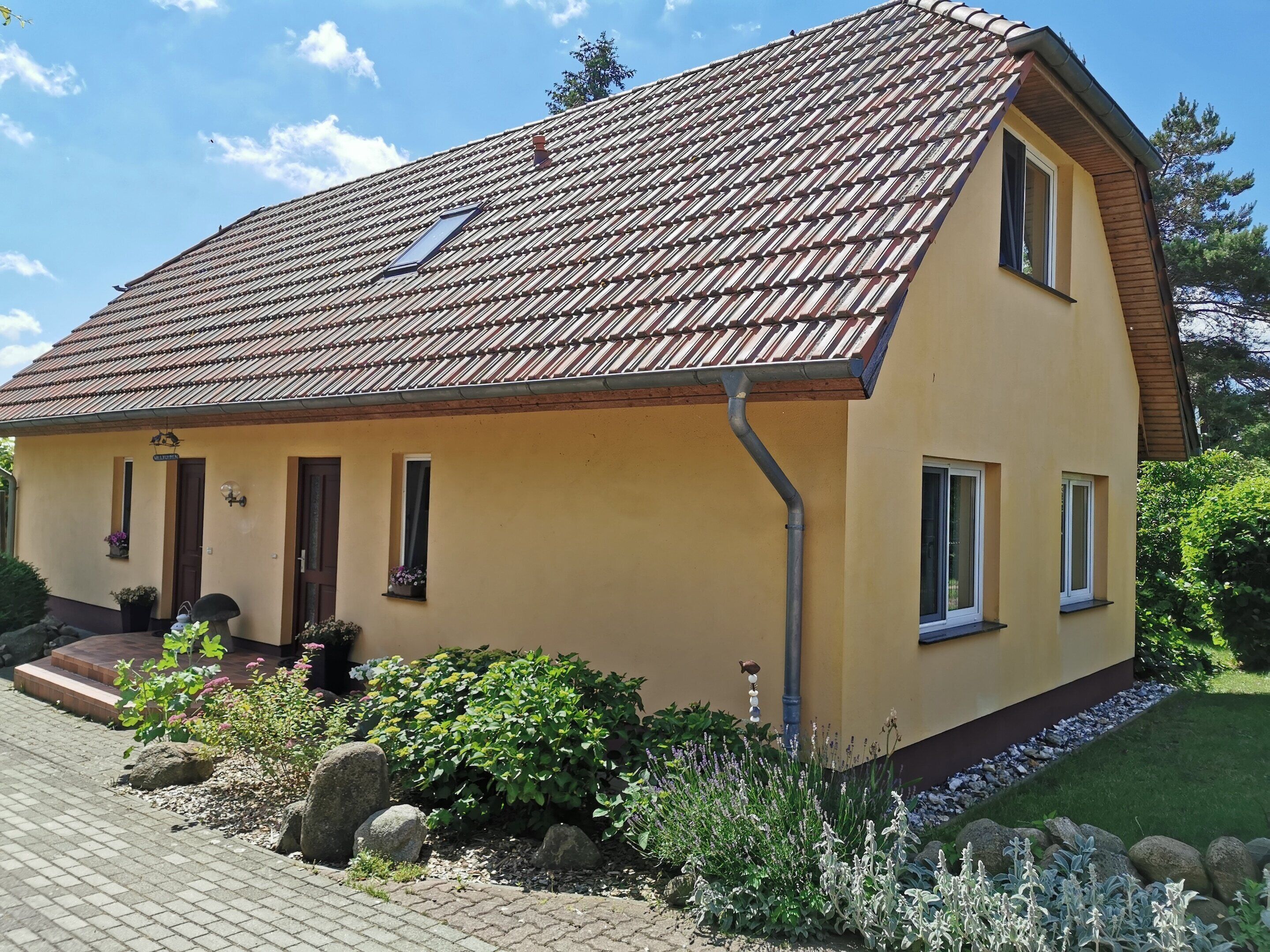 A two-story house with a tiled roof, a front porch, and a small garden with rocks and plants.