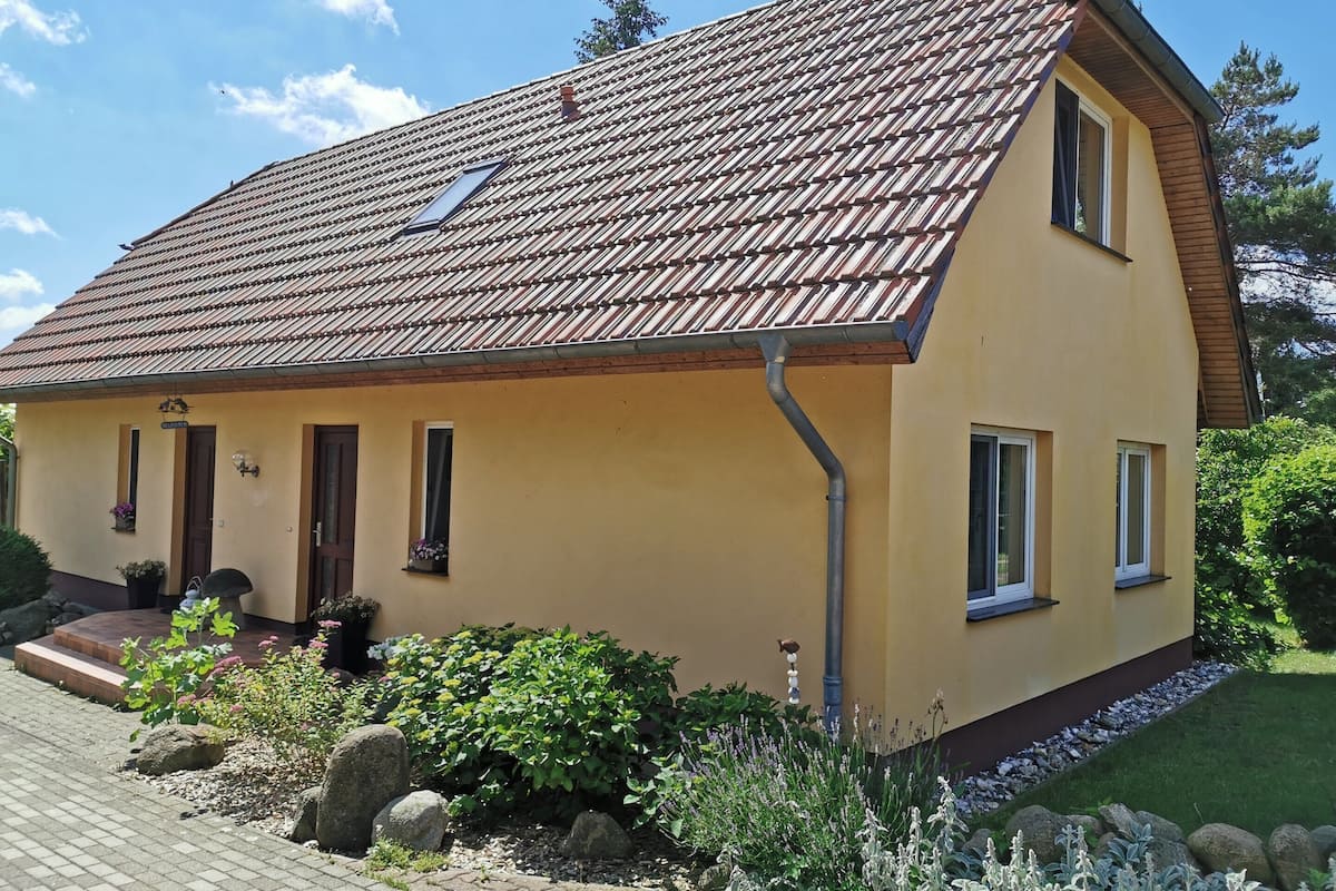 A two-story house with a tiled roof, a front porch, and a small garden with rocks and plants.