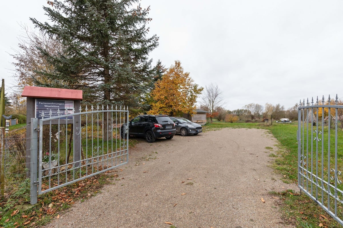 A gravel driveway leading to a gated area with parked cars and a signboard.