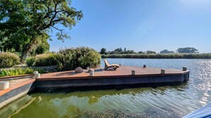 A wooden dock with a lounge chair, surrounded by greenery and a calm body of water. - Spacious Appartment in Wilhelmshof Near Lake (Usedom)