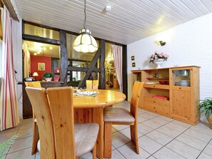 A dining area with a round wooden table and chairs, a hanging light fixture, and a wooden cabinet with glass doors. - Cozy Apartment in Lowensen Lower Saxony With Private Terrace (Bad Pyrmont)