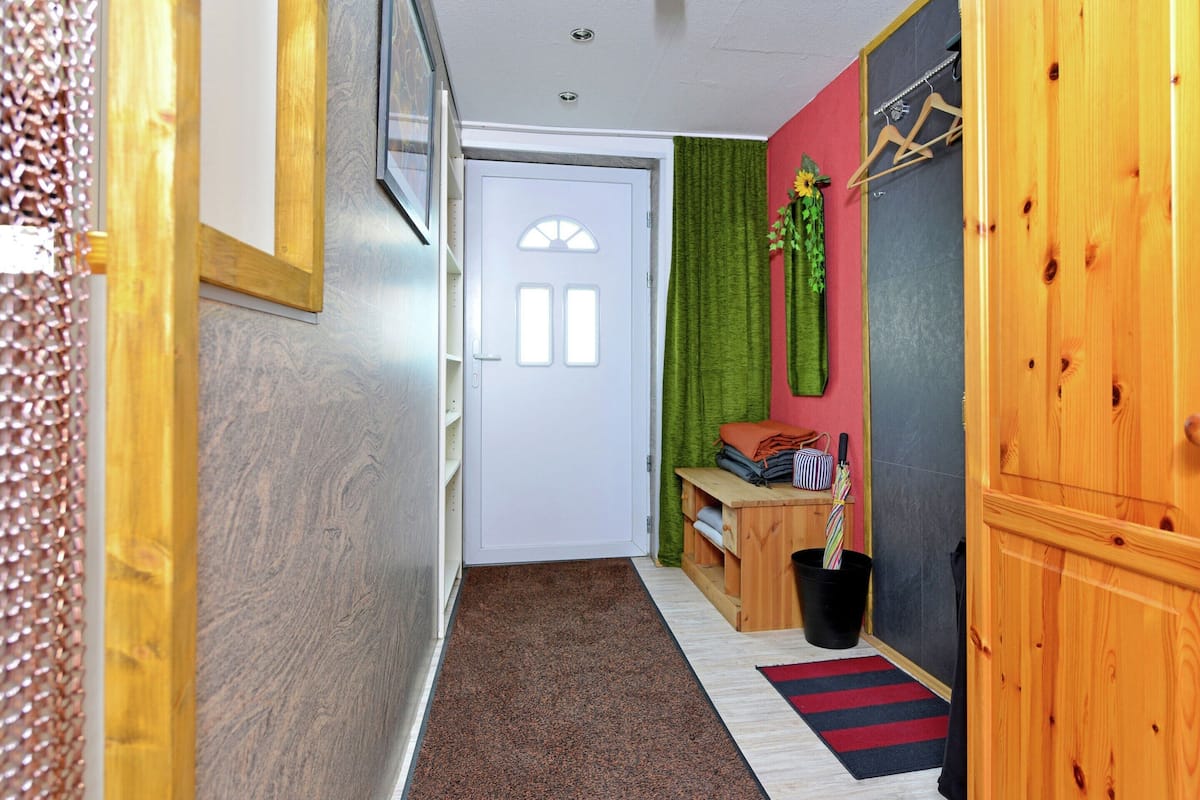 A hallway with a wooden door, a small table with a plant, and a red and black striped rug.