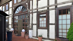Un edificio tradizionale a graticcio con un'ampia finestra ad arco, piante in vaso e una statua sulla facciata.