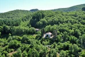 Una piccola casa bianca immersa in una fitta foresta, con vista libera sul verde circostante e sulle colline.