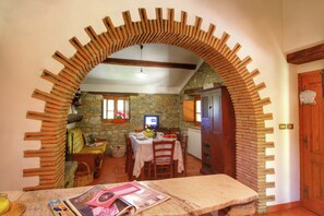 Un'area pranzo con parete in pietra, arredi in legno e un arco in mattoni.