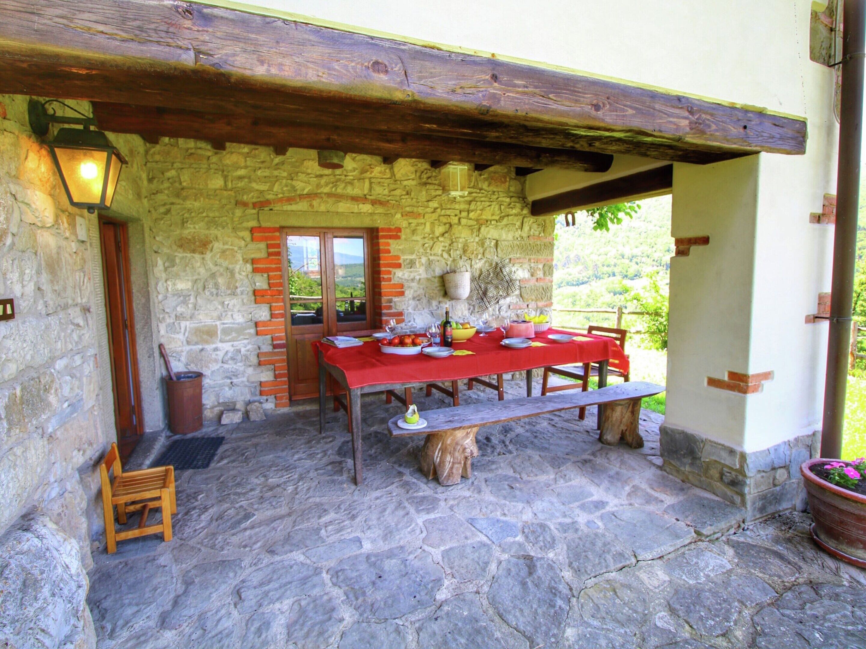 A stone patio with a red table set for dining, wooden benches, and a stone wall with a wooden door.