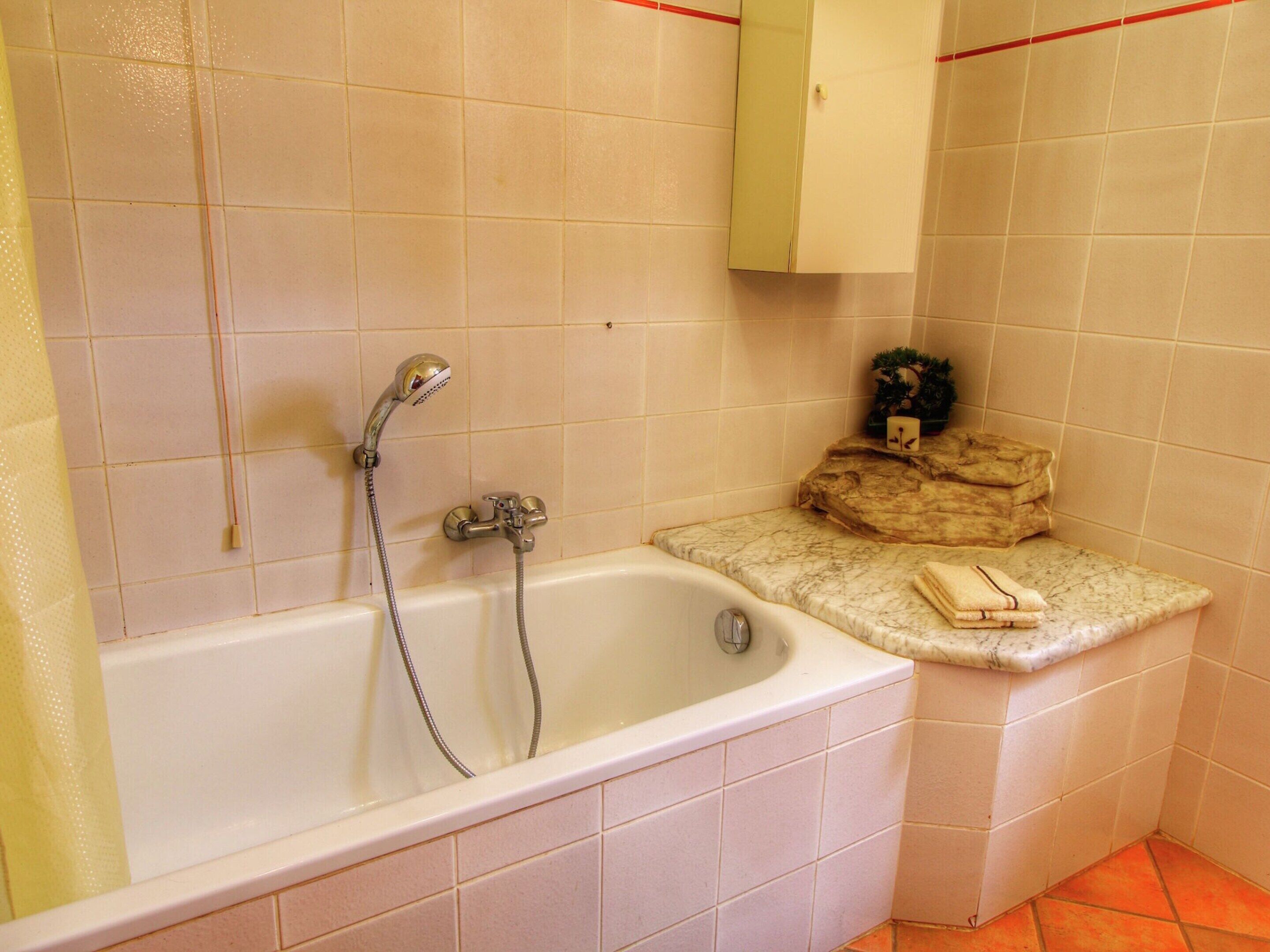 A bathroom with a bathtub, a showerhead, and a towel on the counter.