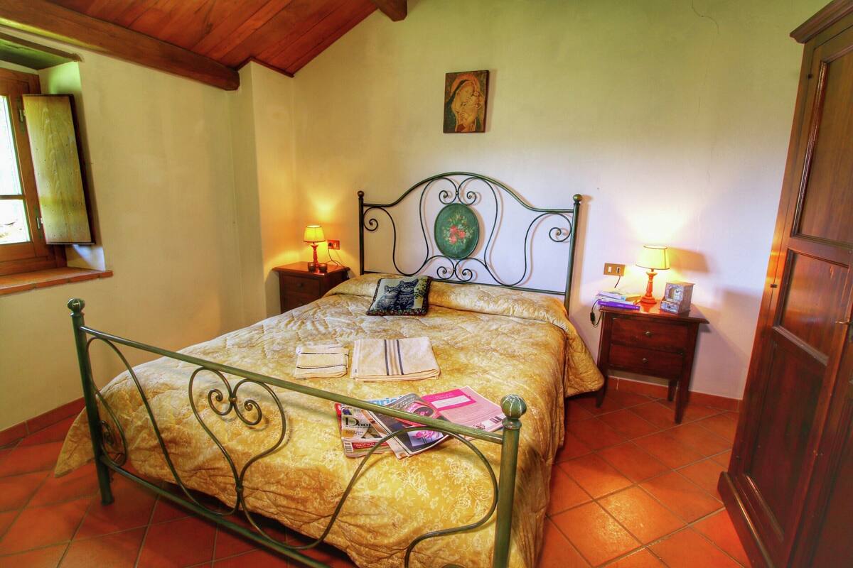 A bedroom with a metal bed frame, a wooden headboard, two bedside tables with lamps, and a wooden wardrobe.