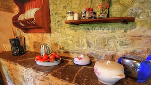 A kitchen counter with a stone backsplash, a coffee maker, a kettle, a bowl of tomatoes, and a shelf with spices and condiments. - Alluring Farmhouse in Ortignano With Swimming Pool (Ortignano Raggiolo)