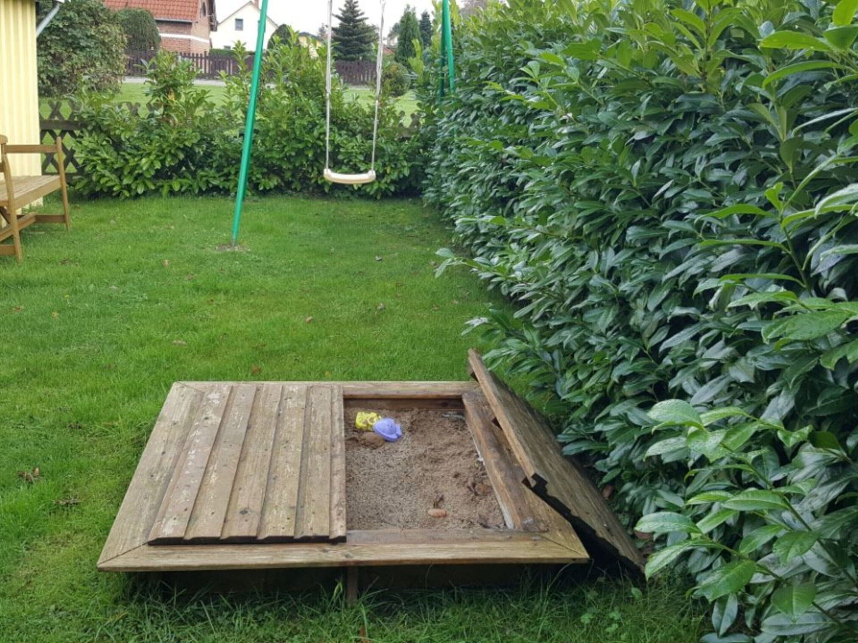 A wooden play area with a swing set and a raised sandbox.