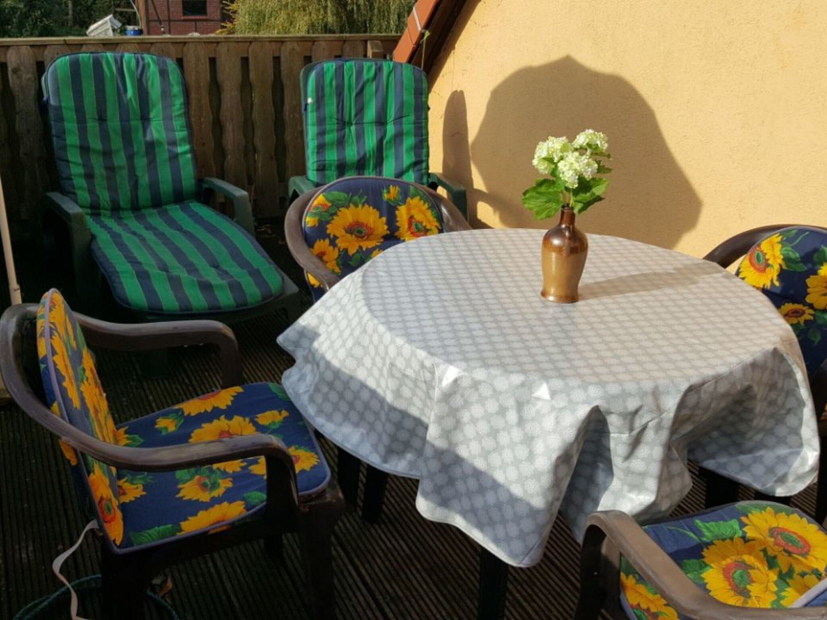 Et rundt bord med hvid dug, omgivet af fire stole med solsikke-betræk.