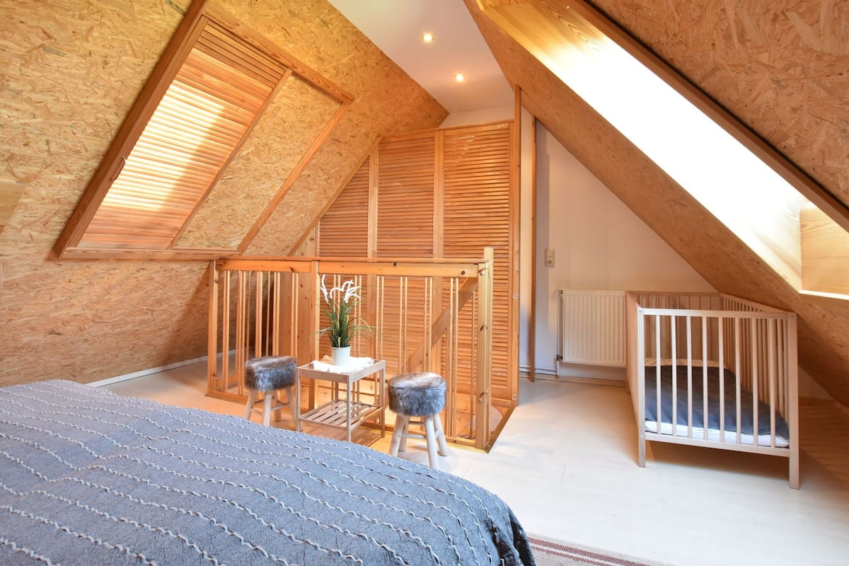 A cozy attic bedroom with a sloped ceiling, a wooden crib, a small table with chairs, and a potted plant.