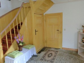 A staircase with a wooden handrail leading to a landing with a white table and a green cushion. A door with a black handle is visible in the background.