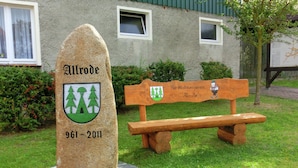 A stone monument with a coat of arms and the inscription "Allrode 961-2011" in a park setting with a wooden bench and a building in the background. - Nice Apartment in Allrode With Private Terrace (Thale)
