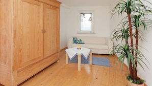 A room with a wooden wardrobe, a small table with a tablecloth, a white sofa, a window, and a potted plant. - Nice Apartment in Allrode With Private Terrace (Thale)
