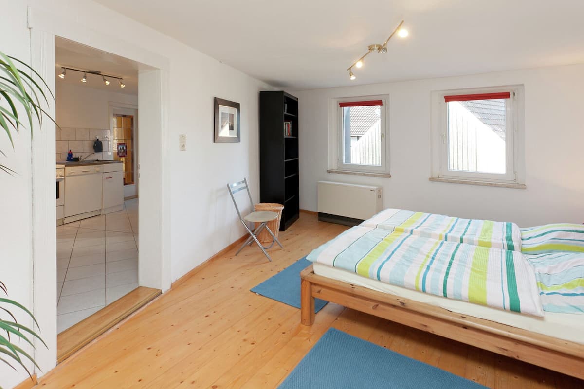 Une chambre à coucher avec un lit en bois, une petite chaise, un radiateur et une fenêtre avec un store rouge.
