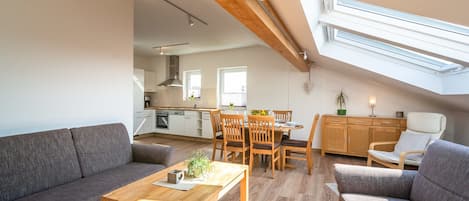A modern loft apartment with a dining area, kitchen, and a large window providing natural light.
