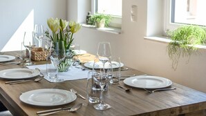 A dining table set with white plates, cutlery, and clear glasses, with a vase of white flowers and a small plant on the windowsill. - Dreamy Holiday Home in Ellscheid With Terrace (Ellscheid)