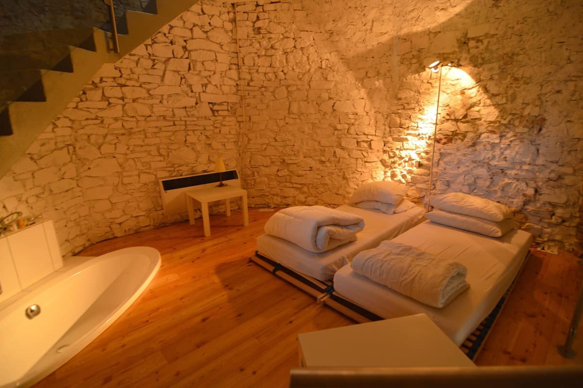 A stone-walled room with a bathtub, two beds with towels, and a staircase.