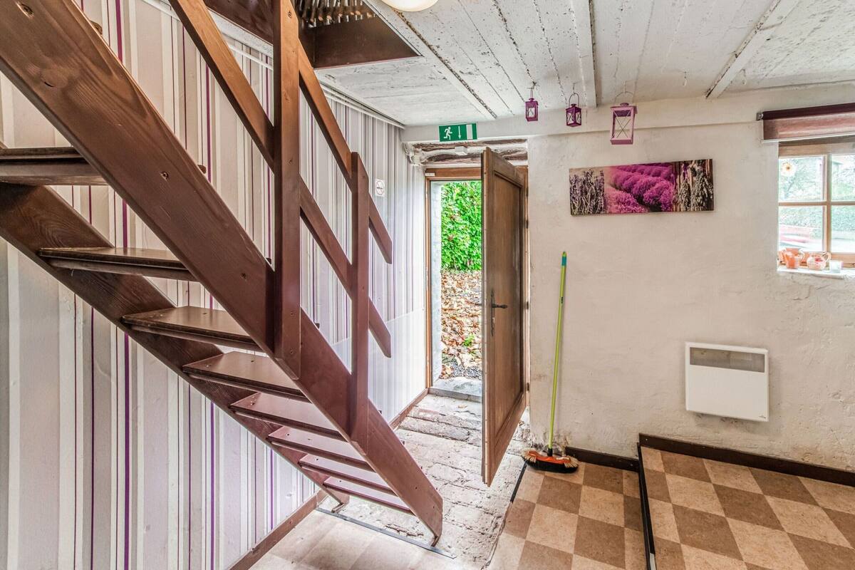 Un escalier en bois menant à une porte sur laquelle est apposée une enseigne verte indiquant la sortie, un balai appuyé contre le mur et un sol à carreaux.