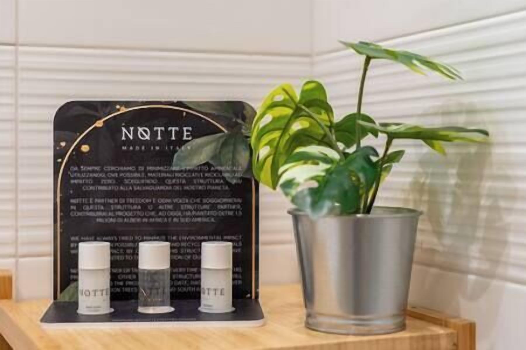 A sign with the word "NOTTE" and three bottles of water on a wooden surface next to a potted plant.