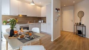 A modern kitchen with white cabinets, a dining table set for two, and a wooden floor.