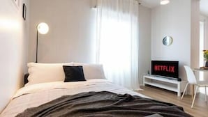 A modern bedroom with a bed, a TV displaying 'NETFLIX', and a white chair.