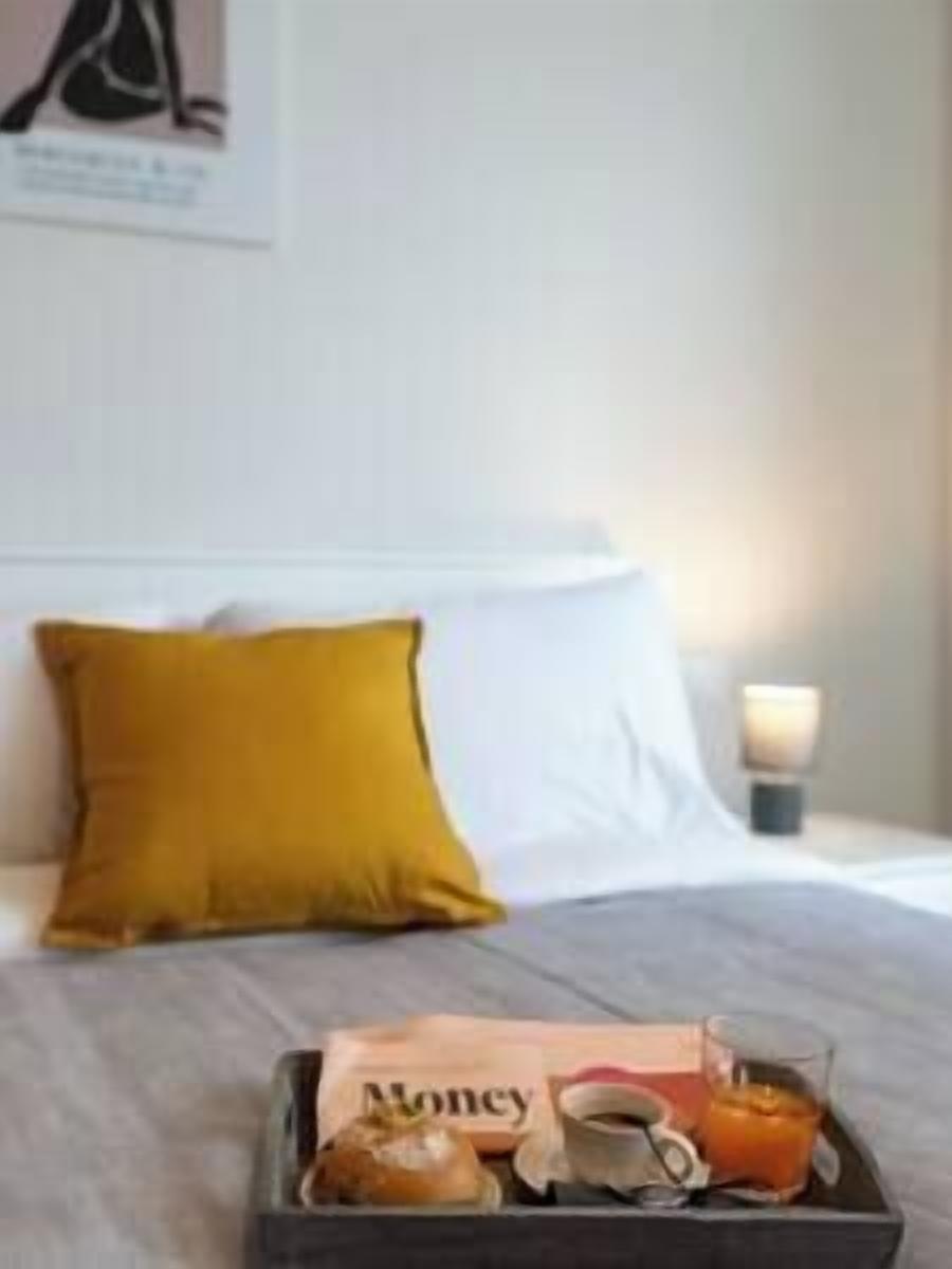 A neatly made bed with a white pillow and a mustard-colored pillow. A tray with a newspaper, a cup, and a glass of orange juice is placed on the bed.