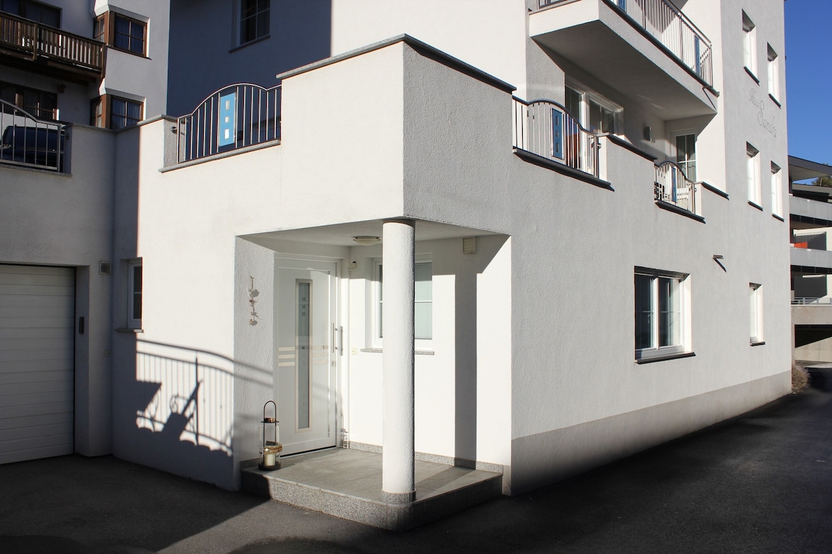 A modern apartment building with a white facade, balconies, and a garage door.