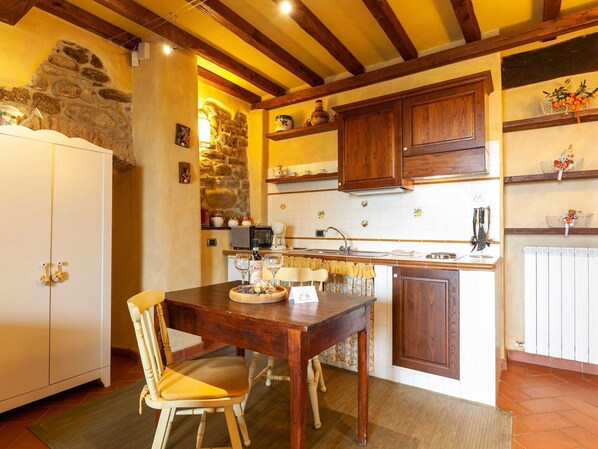 Une cuisine chaleureuse avec des meubles en bois, un mur en pierre et un coin repas comprenant une table et des chaises.