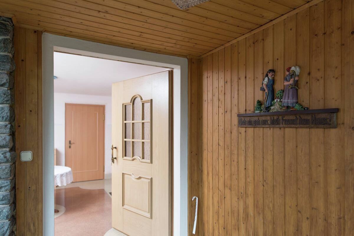 A wooden interior with a door leading to another room, a shelf with figurines, and a stone wall.