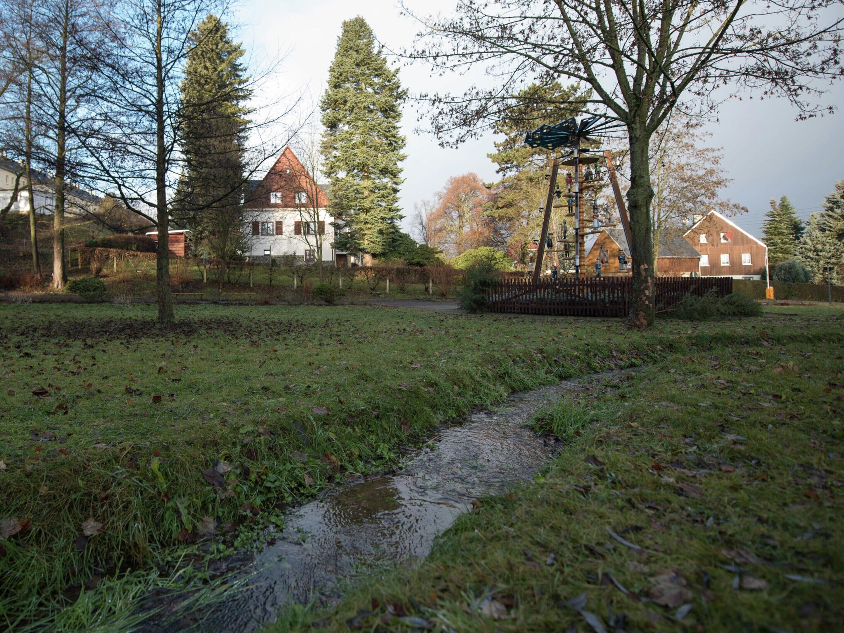 Un paysage rural avec un petit ruisseau, des maisons et des arbres.
