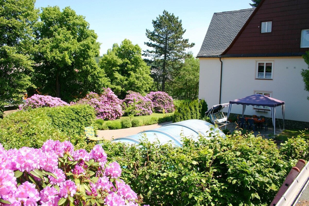 A garden with flowering bushes and a covered outdoor seating area.