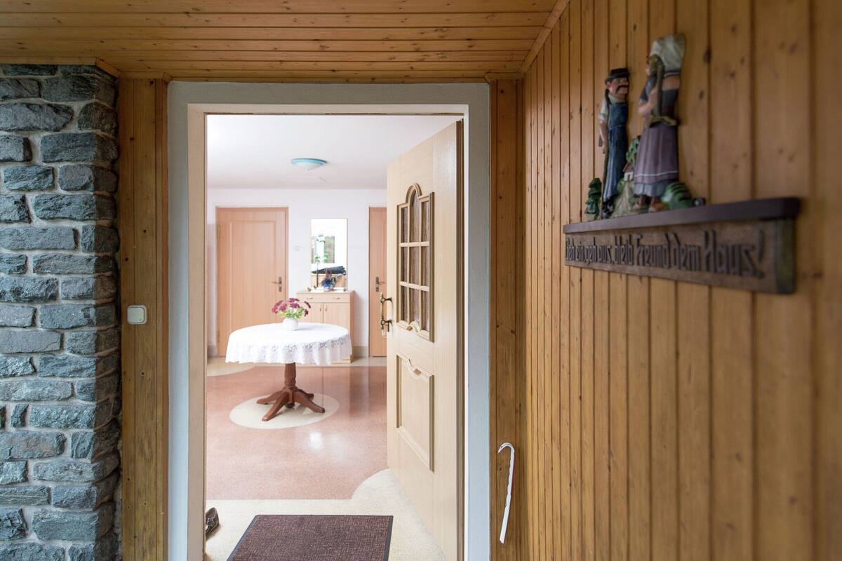 Ein Holzinterieur mit einer Steinwand, einem runden Tisch mit Spitzenbettwäsche und einem Regal mit Figuren.