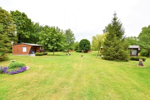 Ein gepflegter Garten mit einer Holzhütte, einem großen Baum und einem kleinen Bauwerk.