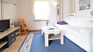 A modern living room with a white sofa, a coffee table, a TV, and a window with blinds. - Boutique Bungalow in Insel Poel With Terrace (Insel Poel)