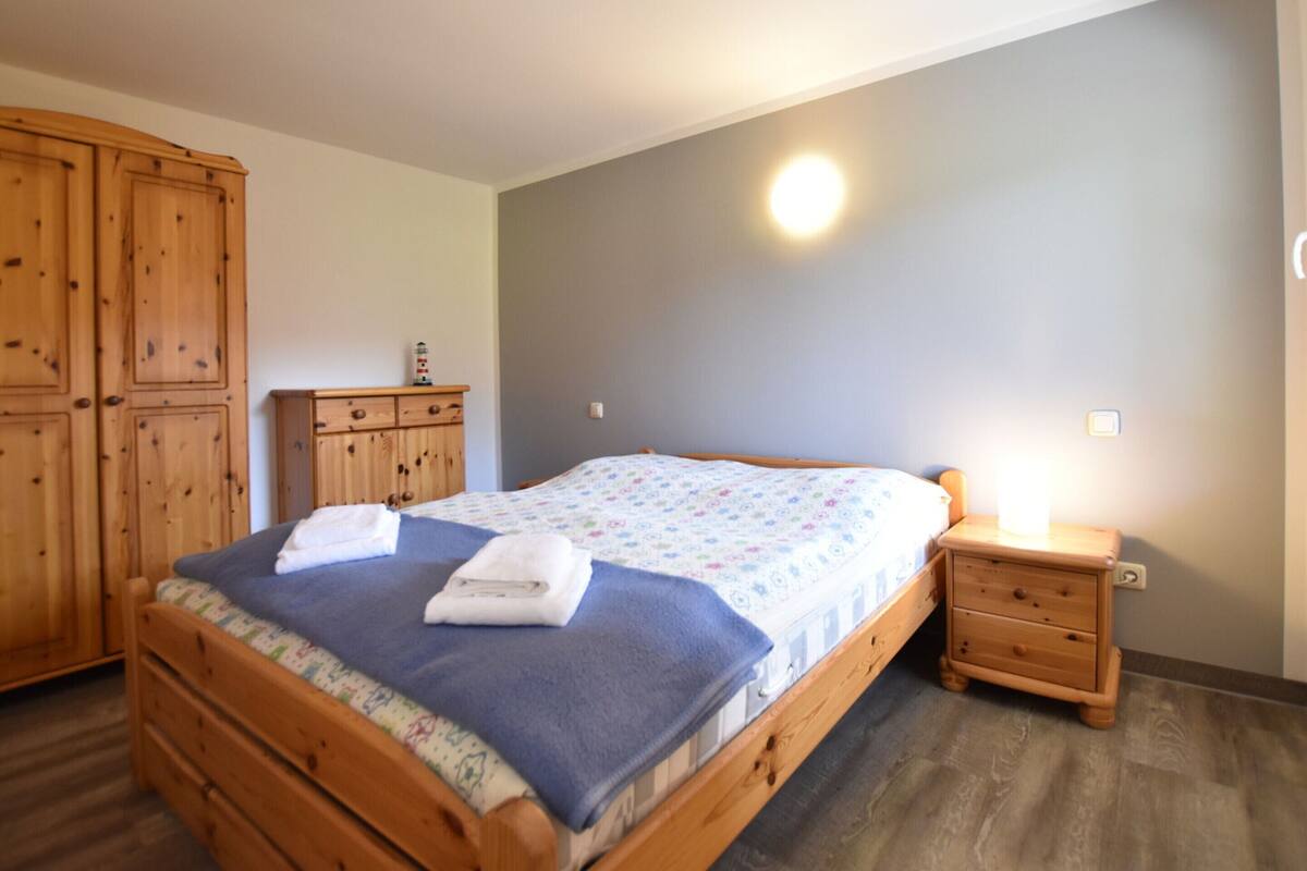 A bedroom with a wooden bed, a nightstand, a wardrobe, and a wall-mounted light.