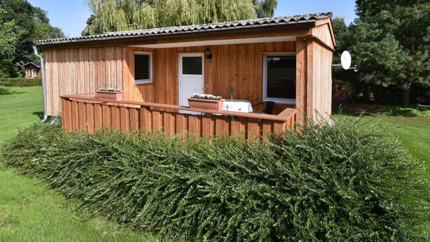 A wooden cabin with a porch, a small window, and a door. - Boutique Bungalow in Insel Poel With Terrace (Insel Poel)