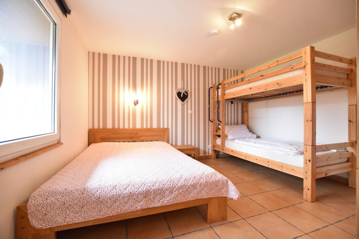 A room with a wooden bunk bed, a single bed, a striped wall, and a heart-shaped decoration.