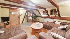 Un salon chaleureux avec un plafond haut, des poutres apparentes, un téléviseur, un canapé et une table basse.