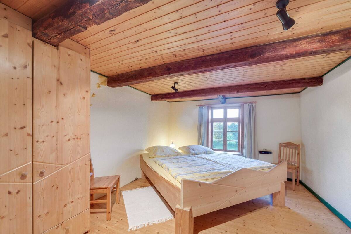 Ein Schlafzimmer mit Holzboden, einem Bett, einem kleinen Holzstuhl und einem Fenster mit Vorhängen.