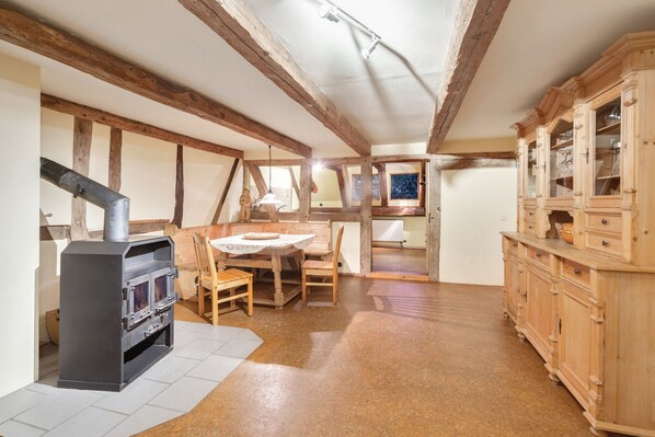 Un intérieur rustique avec des poutres apparentes, une cheminée, une table à manger avec des chaises et un buffet en bois doté de portes en verre.