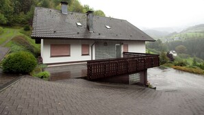 Ein zweigeschossiges Haus mit geneigtem Dach, einem kleinen Balkon und einem gepflasterten Auffahrt.