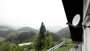 Ein Balkon mit Blick auf ein Tal, eine Satellitenschüssel und ein geparktes Auto davor.