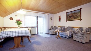 Ein gemütliches Zimmer mit Esstisch, zwei Sesseln, einer Couch, einem Heizkörper und einem Kruzifix an der Wand.